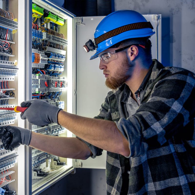 Male electrician working in switchboard with electrical connecting cable. Electrical engineer in special clothes with flashlight on helmet in dark room with emergency lights. Space for text. SSUCv3H4sIAAAAAAAAA41Py46DMAz8F5+DBIUtLL9S9RASA1EDQYmzVYXy7+tQqr1uTvaMM48djIYe6rFsq0aVhS5VV1QVjsXwXcpCtU2DXd2pq9IgQEtC6Ku67qpLXX9dumvblvwEDDIYBf0OxtoYyEsyboWeGY+rRn+MqA05b6TlLQkIJCkGDPyNN8XaE7PH/tG77RnngGwe4pCHJP6J3QXICVf1yvopB7EoD7sbU48noV9Ob0dzjsgiLq7kX28h69wmB8uNR2kDCphlCHygT4A/bt4os05nAy7ulve8OspORx5y6mH0afUuPRtGs88OcbNOatQnHYfFEH1Wjz8Gn3/XKaVfiV598rIBAAA=